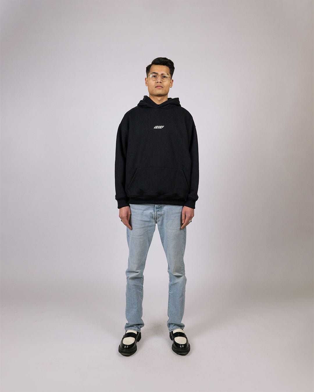 Essential Hoodie Black - Relaxed Fit with embroidered graphic, worn model.