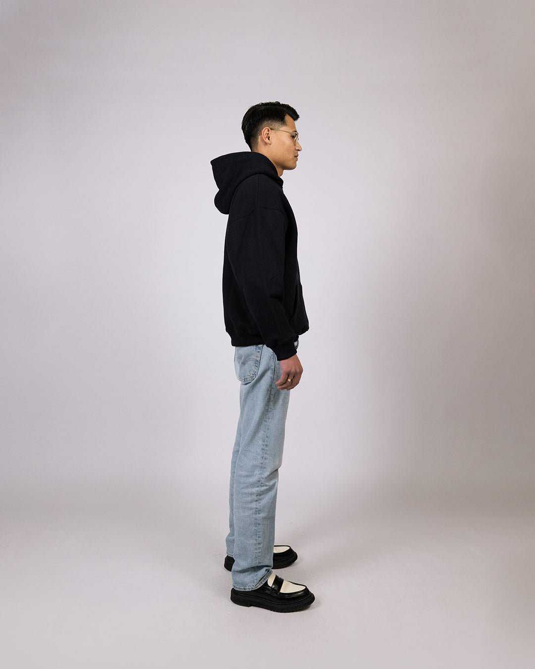 Essential Hoodie Black in relaxed fit with embroidered graphic, side view.