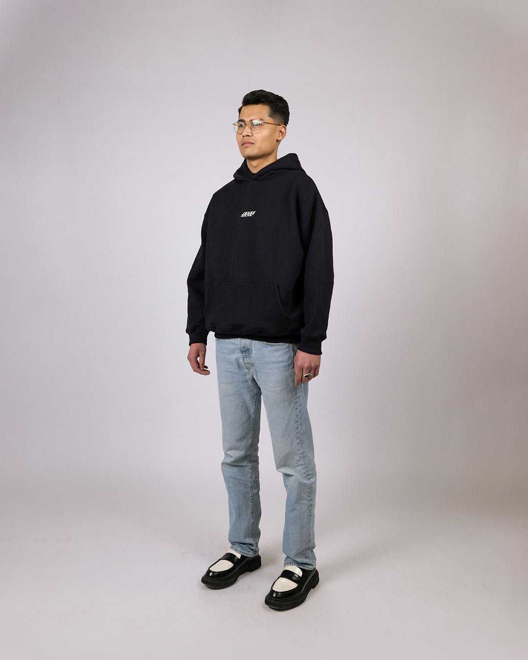 Essential Hoodie Black - Relaxed Fit with embroidered graphic, modeled by person wearing size M.